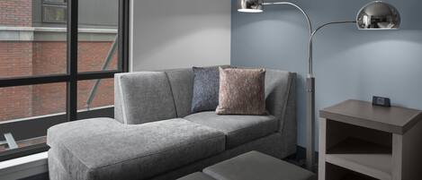 Una sala moderna con un sofá gris, dos otomanas, una mesita auxiliar y una lámpara de pie.