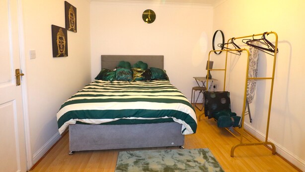 Ein Schlafzimmer mit einem Bett, einer Bank, einem Kleiderständer und einer Wanduhr.