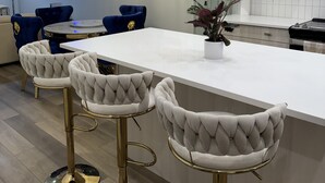 A modern kitchen with a central island, bar stools, pendant lights, and a dining area with a sofa and chairs. - Luxury Home with Hot Tub, a stunning haven with 3 bedrooms and 2.5 bath (Calgary)