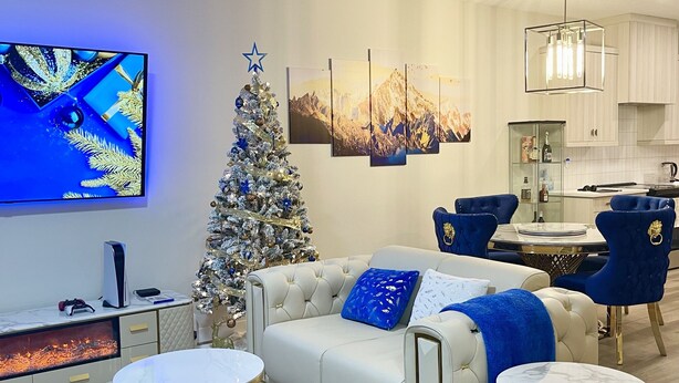 A modern living room with a white sofa, blue accents, a Christmas tree, and a flat-screen TV. - Luxury Home with Hot Tub, a stunning haven with 3 bedrooms and 2.5 bath (Calgary)
