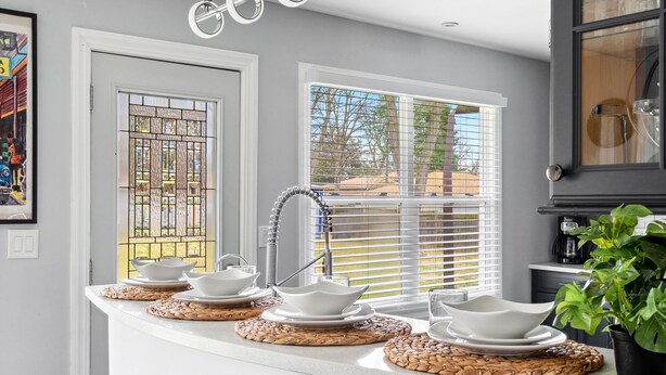 A kitchen with a white countertop, four stools, a hanging light fixture, and a window with blinds. - Spacious Home in Chicago Suburbs (Lombard)