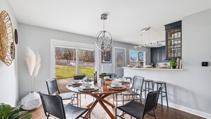 A dining area with a round table set for six, surrounded by black chairs. There is a large window with a view of the outdoors. - Spacious Home in Chicago Suburbs (Lombard)