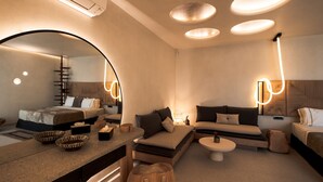 A modern hotel room with a bed, sofa, and a dining area. There are multiple light fixtures and a large mirror. - Brilliant Topaz Suite with Private Pool (Mykonos)