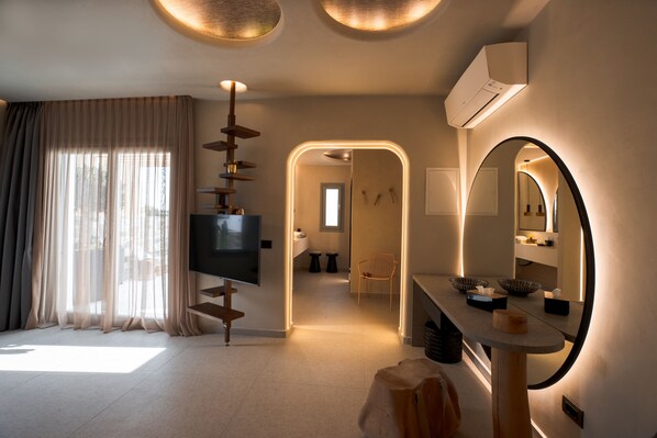 Une chambre d’hôtel moderne équipée d’une grande télévision, d’un miroir et d’un bureau avec un bol et des mouchoirs.