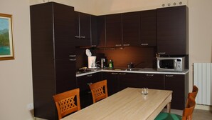 Een compacte keuken met donkere kastjes, een magnetron, een spoelbak en een eettafel met stoelen.