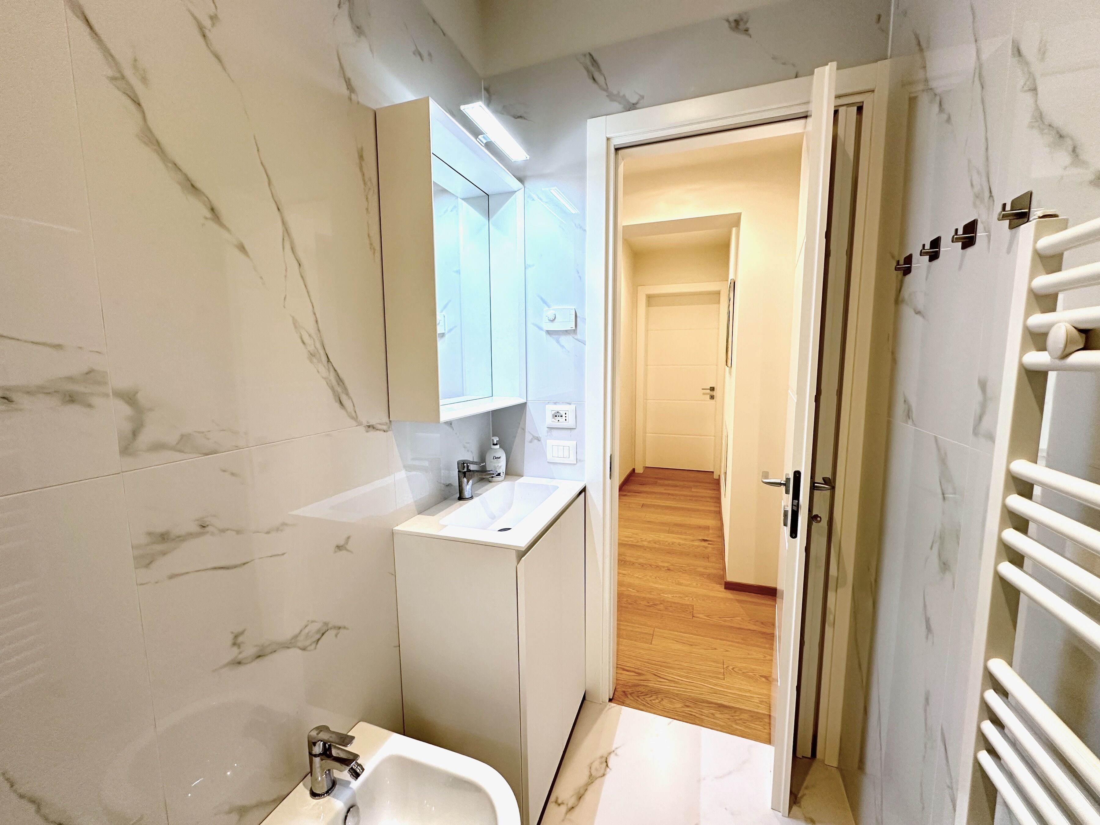 Un bagno moderno con rivestimento in marmo, un lavandino bianco e uno specchio.