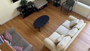 Ein Wohnzimmer mit Sofa, Couchtisch, Fernseher, Pflanze und Fenster.