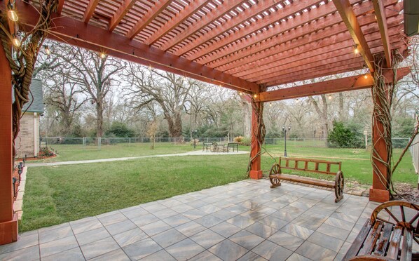 A covered patio with a bench, a paved area, and a view of a grassy yard and trees. - Chick & Modern Getaway Ranch - Lake Livingston View! (Point Blank)