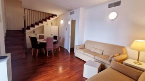 Ein modernes Wohnzimmer mit Holzboden, einer Couch, einem Esstisch mit Stühlen und einer Treppe, die zu einer anderen Ebene führt.