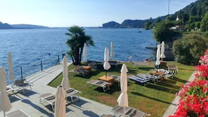 Eine Uferterrasse mit Liegestühlen und Sonnenschirmen mit Blick auf ruhiges Wasser und Hügel in der Ferne.