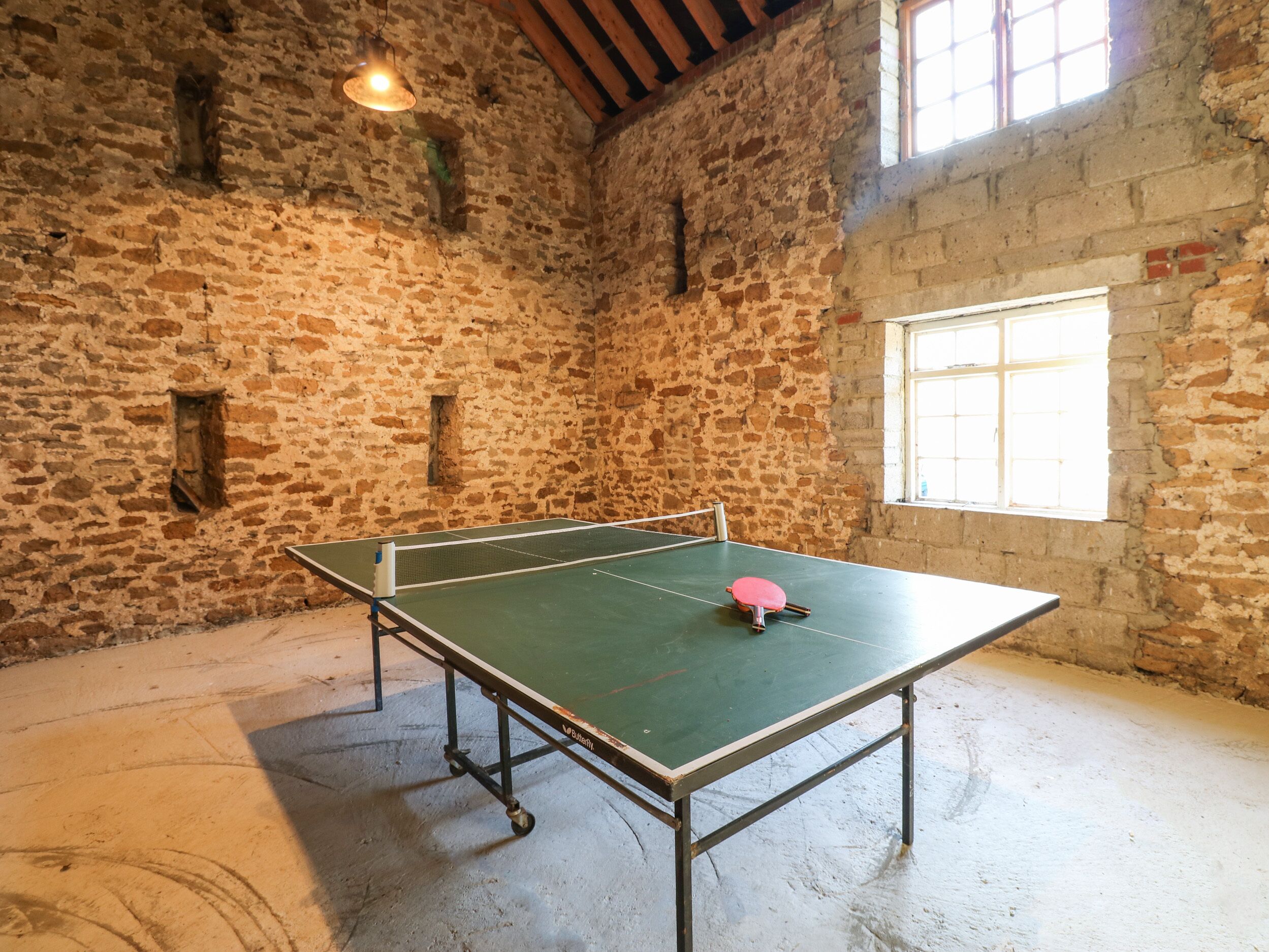 Egy pingpongasztal egy olyan szobában, amelynek kőfalai és egy ablakja van.