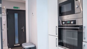 A modern kitchen with stainless steel appliances, a fire exit sign, and a trash bin.