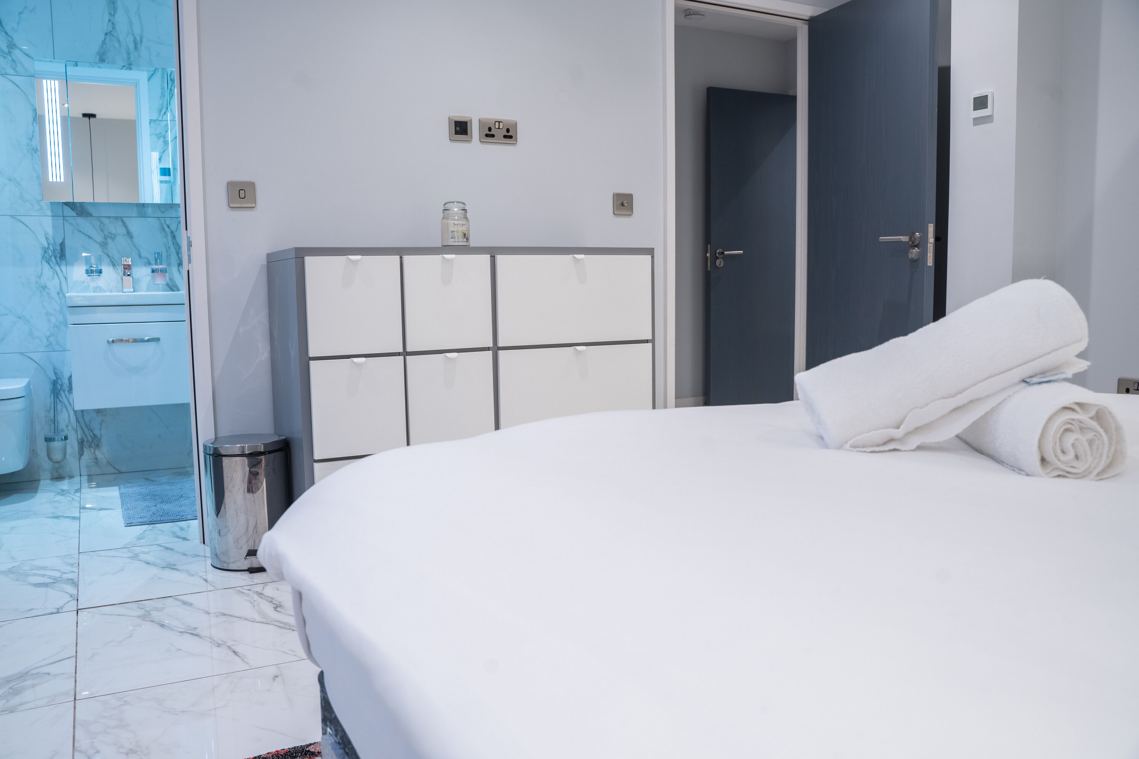A hotel room with a large bed, a wardrobe, a bathroom with a mirror, and a door leading to another room.