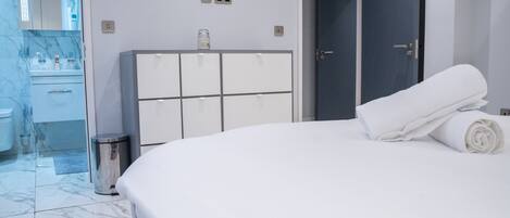 A hotel room with a large bed, a wardrobe, a bathroom with a mirror, and a door leading to another room.
