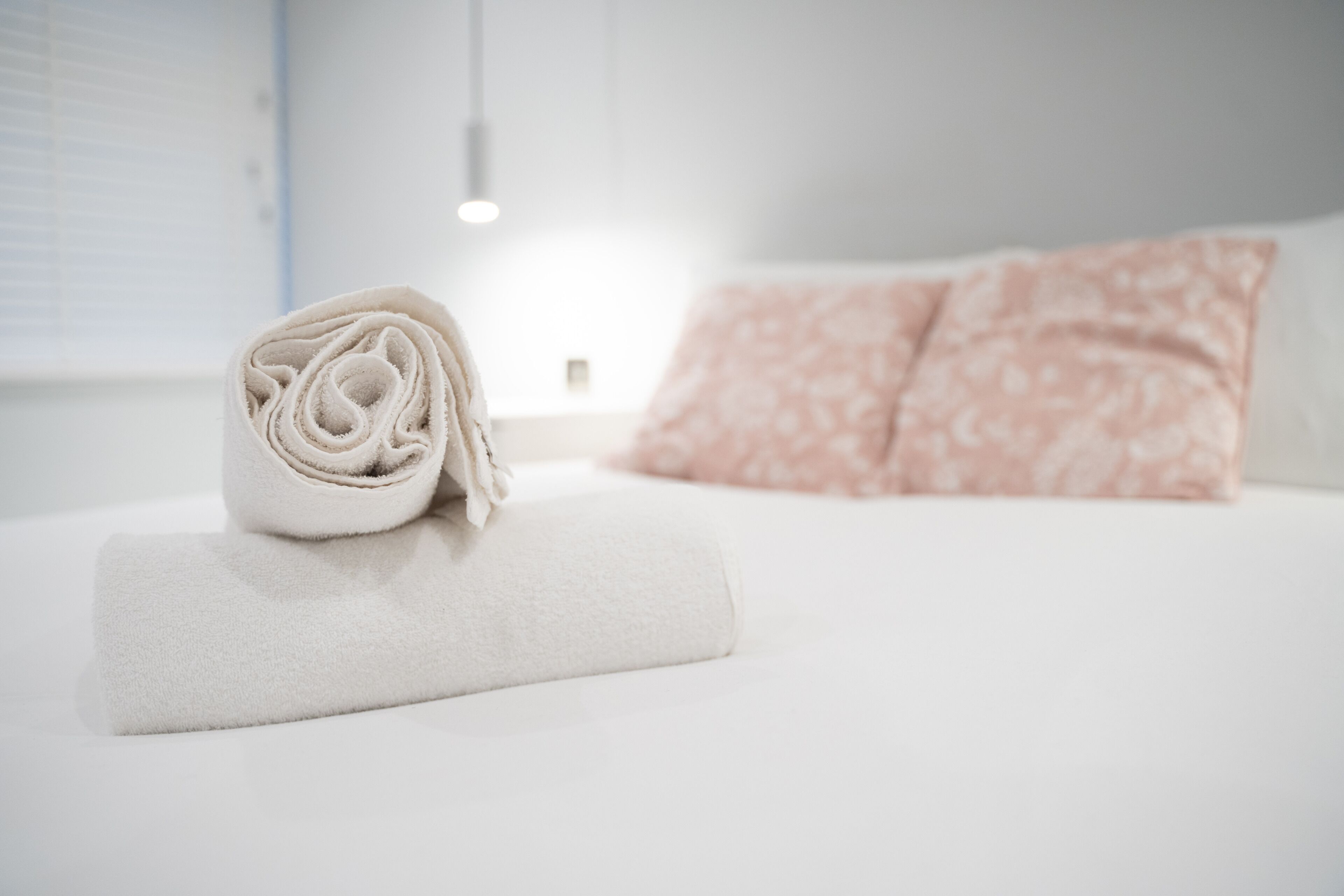 Een netjes opgemaakt wit handdoek op een bed met een wit en roze bloemenkussen.