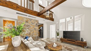 A spacious living room with a stone accent wall, a wooden staircase, a large TV, and a cozy seating area. - 3-bedroom vacation home just 12 minutes from Lafayette and Lehigh College. (Nazareth)