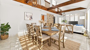 Un vaste espace dédié à la salle à manger, avec une table et des chaises en bois, un mur décoratif en pierre et un escalier dont les poutres apparentes sont mises en valeur.