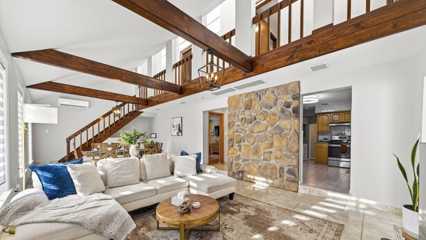 A spacious living area with a high ceiling, exposed wooden beams, a stone accent wall, and a view into the kitchen. - 3-bedroom vacation home just 12 minutes from Lafayette and Lehigh College. (Nazareth)