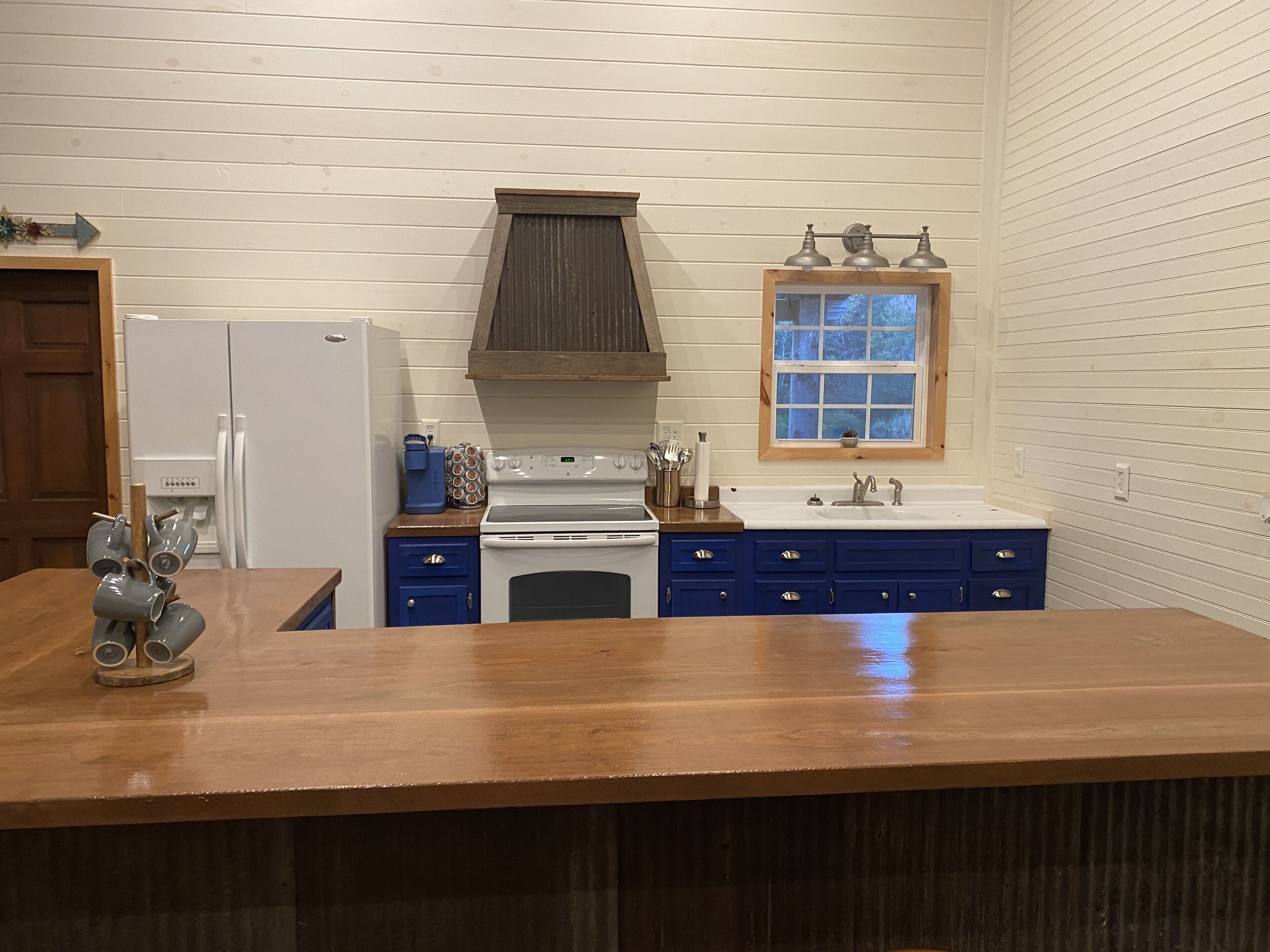 Een keuken met een houten aanrecht, witte apparatuur, blauwe kastjes en een raam met uitzicht.