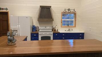 Een keuken met een houten aanrecht, witte apparatuur, blauwe kastjes en een raam met uitzicht.