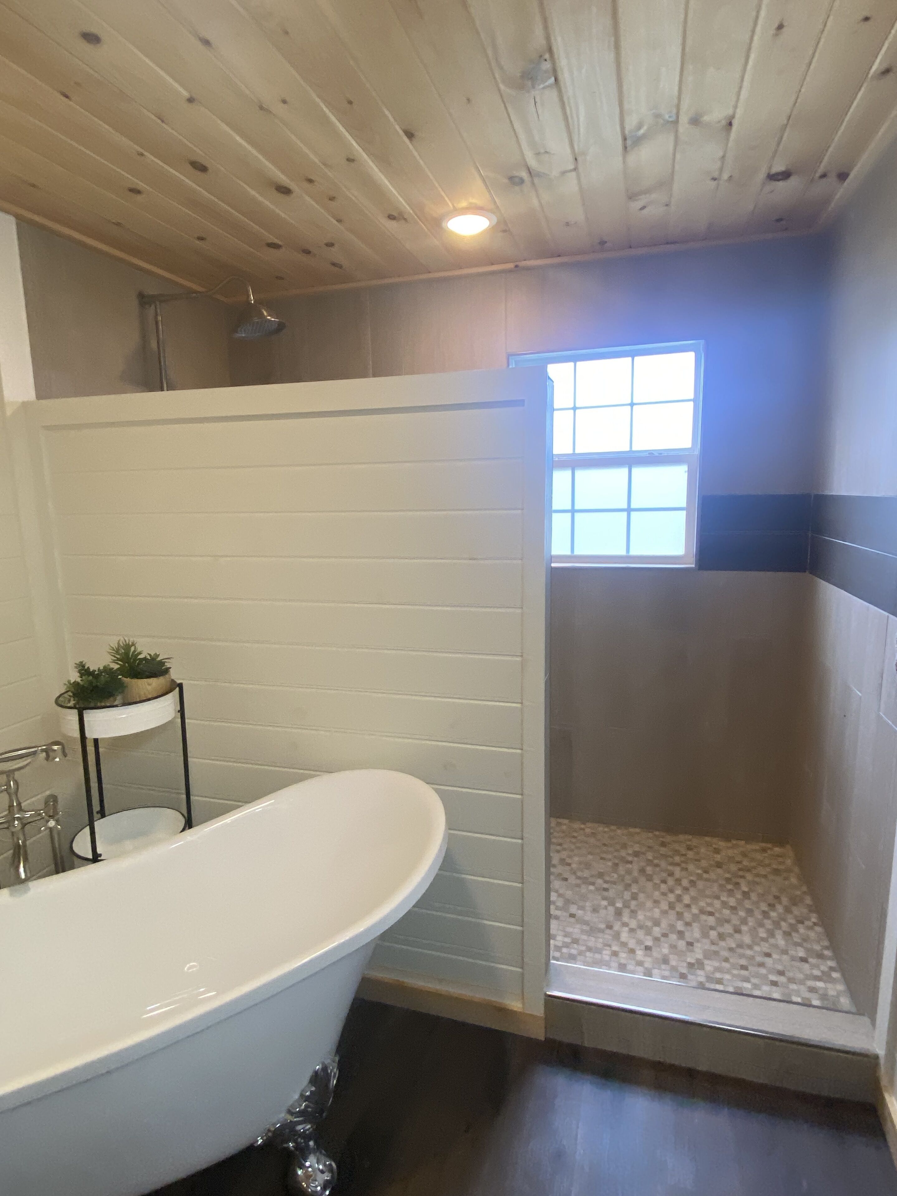 A bathroom with a freestanding bathtub, a shower enclosure, and a small window.