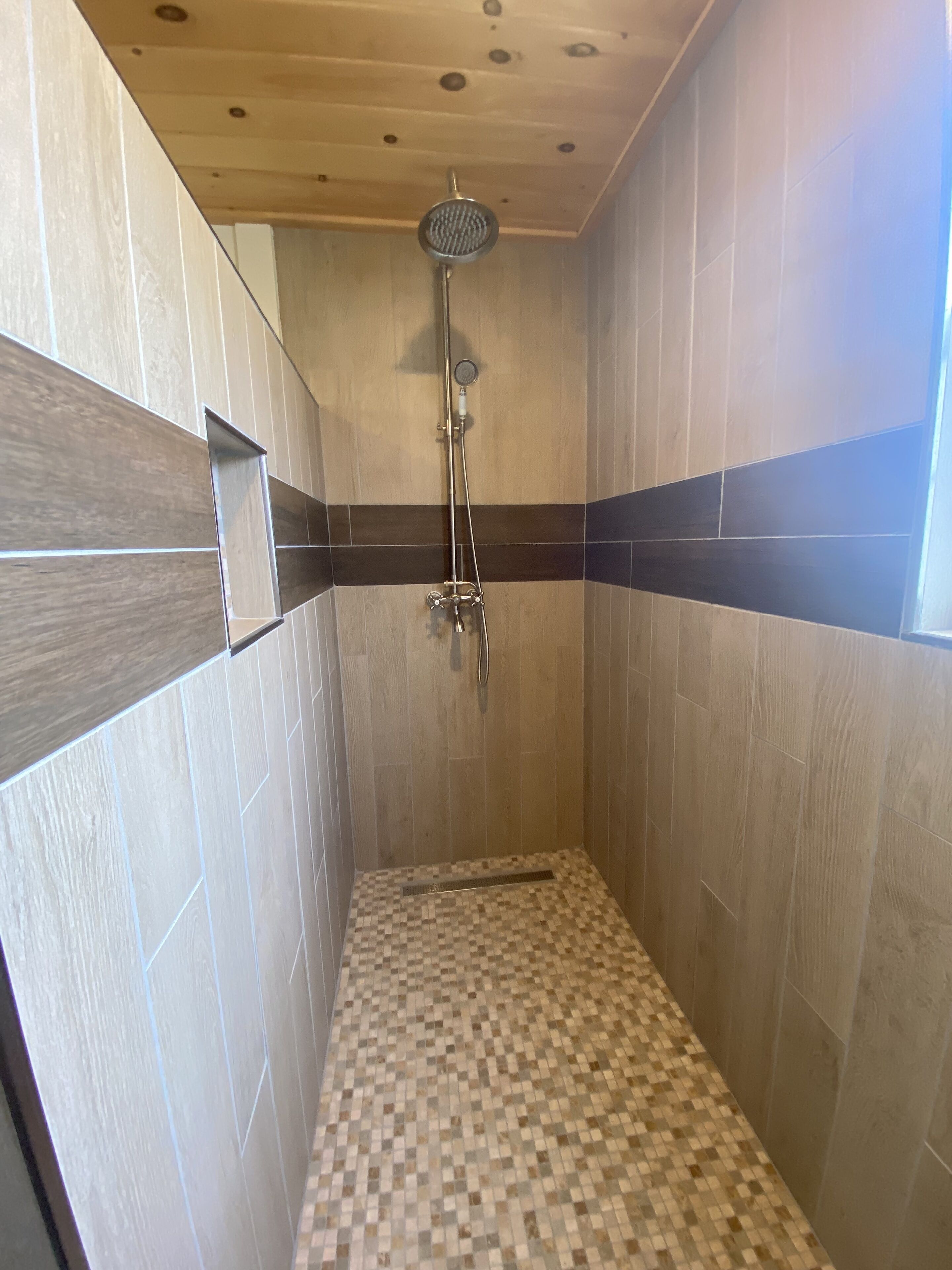 Un área de ducha con paredes y piso de azulejos, y techo de madera.