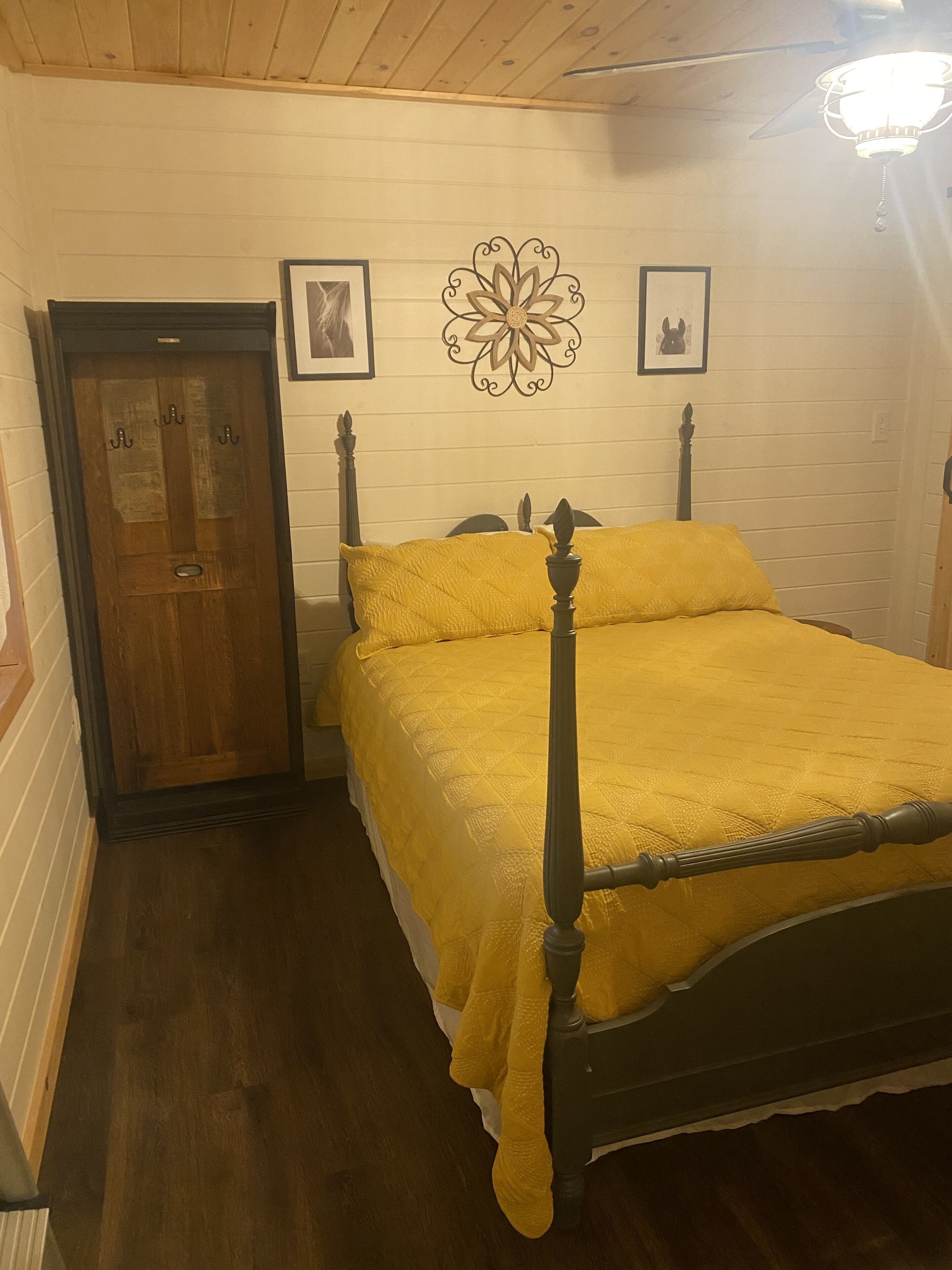 Camera da letto con struttura letto in legno, copriletto giallo, porta in legno e un lampadario a parete.