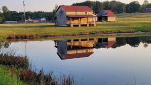 Ein hölzernes Bauernhaus mit rotem Dach, eine kleine Werkstatt und ein Teich, der die Gebäude spiegelt.
