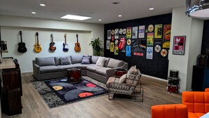 A modern living room with a sectional sofa, a drum set, and guitars on the wall. - Prime Downtown Music Lovers Experience! Nostalgic Mid-Mod In Historic St Peter (Saint Peter)