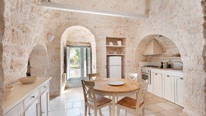 A rustic kitchen with stone walls, a round wooden table, and white cabinets. - Trulli Bellavista Pool - Cocolic... (Cocolicchio)