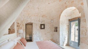 A stone-walled bedroom with a bed, pillows, a lamp, and a window. - Trulli Bellavista Pool - Cocolic... (Cocolicchio)