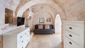 A stone-walled room with a sofa, a TV mounted on the wall, and a cabinet with drawers. - Trulli Bellavista Pool - Cocolic... (Cocolicchio)