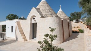 A small, white stone building with a conical roof, a staircase leading to an entrance, and a small tree in the foreground. - Trullo Dei Ricordi - Cisternino (Cisternino)