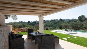An outdoor patio with wicker furniture, a table, and a view of a swimming pool and greenery. - Trullo Dei Ricordi - Cisternino (Cisternino)