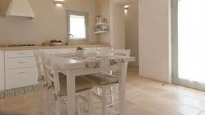 A kitchen with white cabinetry, a dining table with chairs, a window with curtains, and a tiled floor. - Trullo Dei Ricordi - Cisternino (Cisternino)