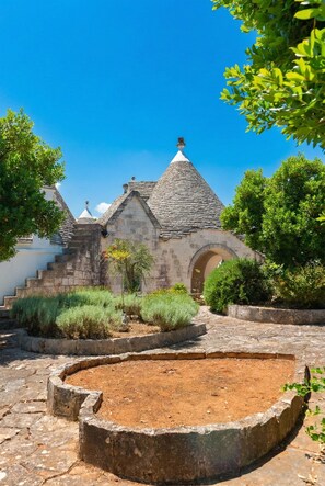 Un bâtiment en pierre surmonté d’un toit conique, entouré de verdure et agrémenté d’un élément décoratif circulaire en pierre.