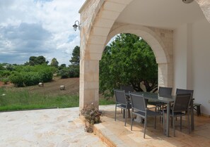 An outdoor patio with stone flooring, a table with chairs, and a stone archway.