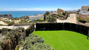 Eine Küstenwohngegend mit gepflegtem Rasen, Gebäuden im mediterranen Stil und freiem Blick auf das Meer.