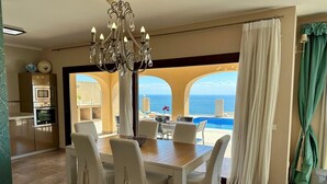 Ein Essbereich mit Tisch und Stühlen, einer Kandelaber und Blick auf den Ozean durch große Fenster.