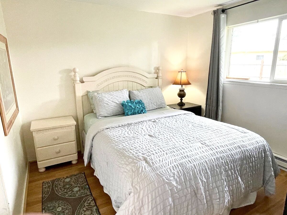 A neatly arranged bedroom with a bed, bedside table, lamp, and a small nightstand.