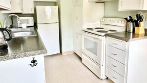 Une cuisine compacte avec des meubles blancs, un four à micro-ondes encastré, une cuisinière et un évier.