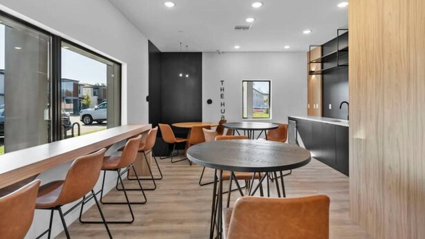 Ein modernes Interieur mit einer langen Theke, mehreren Tischen, Stühlen, einer Küchenzeile und einem großen Fenster mit Blick nach draußen.
