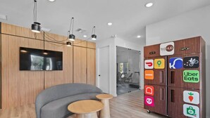 Ein moderner Arbeitsbereich mit einem grauen Sofa, Holztischen und einem an der Wand montierten Fernseher.