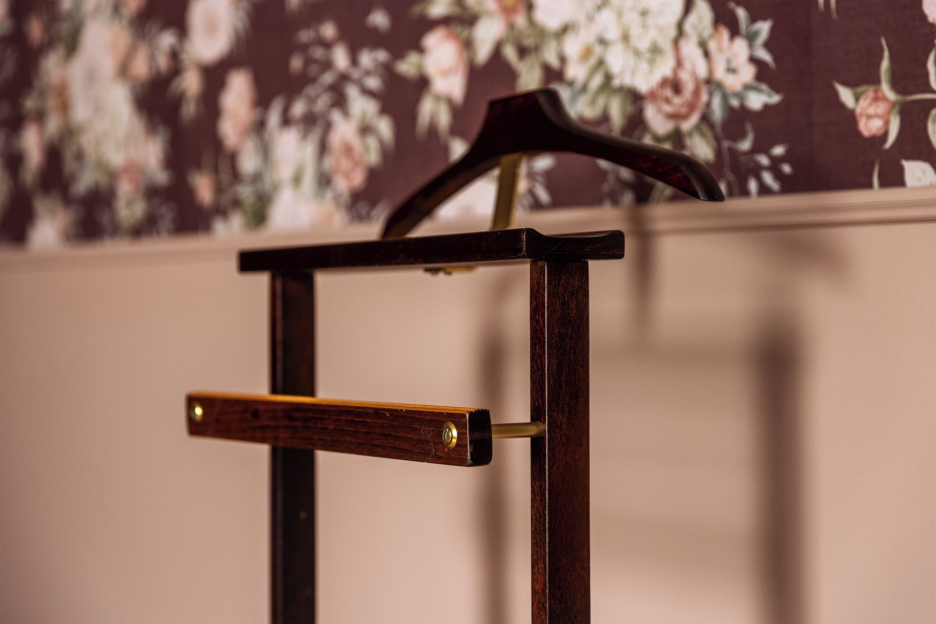 A wooden chair with a metal armrest against a floral wallpaper background.
