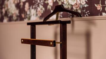 A wooden chair with a metal armrest against a floral wallpaper background.