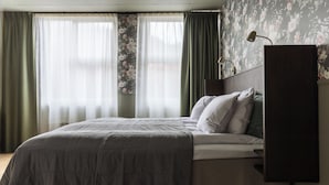 A bedroom with a bed, a nightstand, a lamp, and a window with curtains.