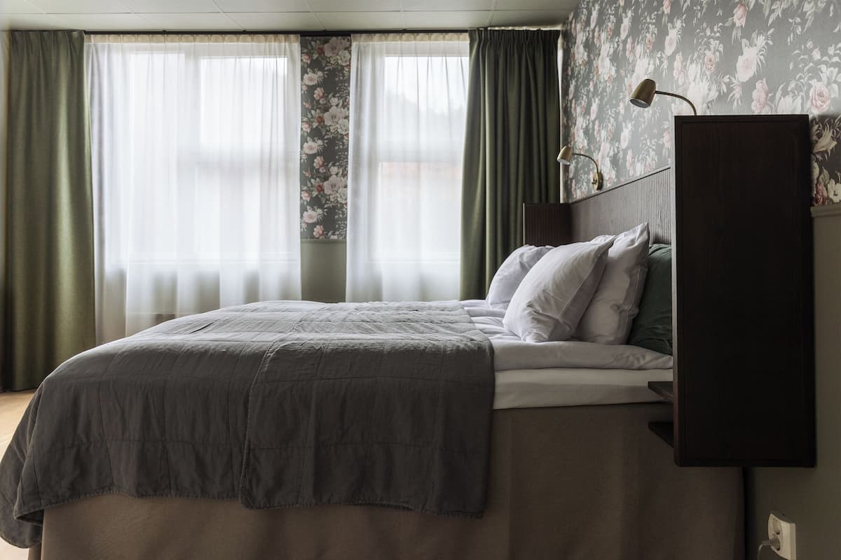 Une chambre à coucher avec un lit, une table de chevet, une lampe et une fenêtre avec des rideaux.