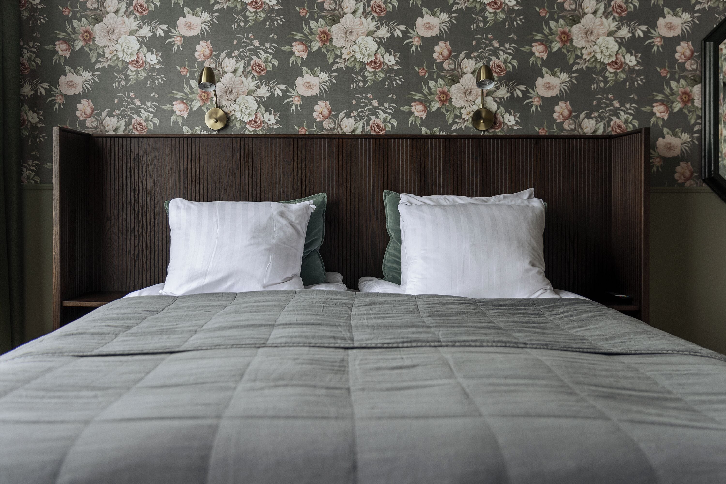 Una cama bien hecha con un edredón gris, dos almohadas blancas y un cabecero de madera oscura.