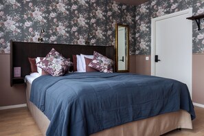 Un dormitorio con cama, papel tapiz floral, un espejo y una puerta.