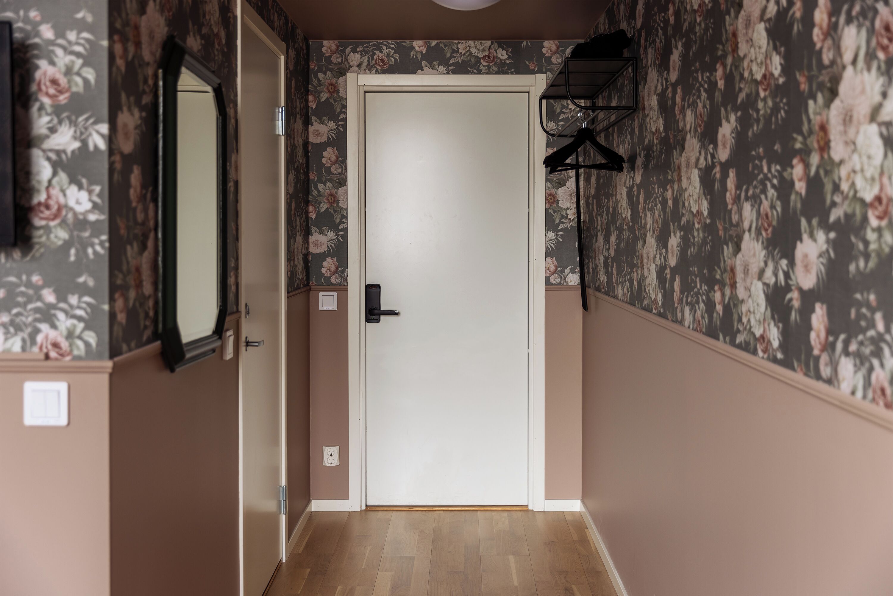 A hallway with floral wallpaper, a white door, and a wooden floor.